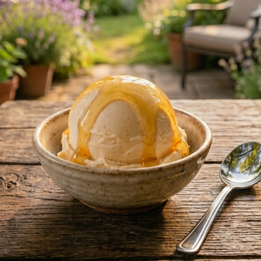 Eine Kugel Honig-Eis, selbstgemacht ohne Eismaschine, in einer Keramikschale auf einem Holztisch im Garten