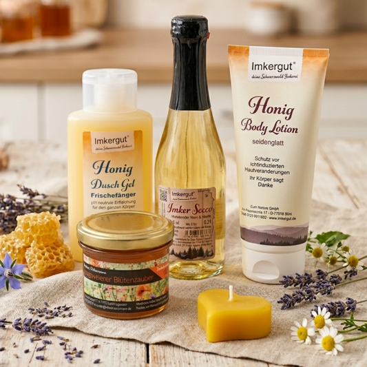 Geschenkset zum Muttertag der Imkerei Ostermann, bestehend aus: 150g Blütenhonig, Imker Secco 0,2l, Honig Body Lotion, Honig Dusch Gel, handgegossene Herz-Kerze aus Bienenwachs auf einem Tisch mit Blütendeko.