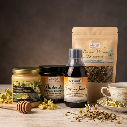 Naturprodukt-Set Erkältungsbegleiter von Imkerei Ostermann mit Lindenblütenhonig, Propolissirup, Gelée Royale Badesalz und Bienenwiesen Kräutertee auf einem gemütlichen Holztisch.