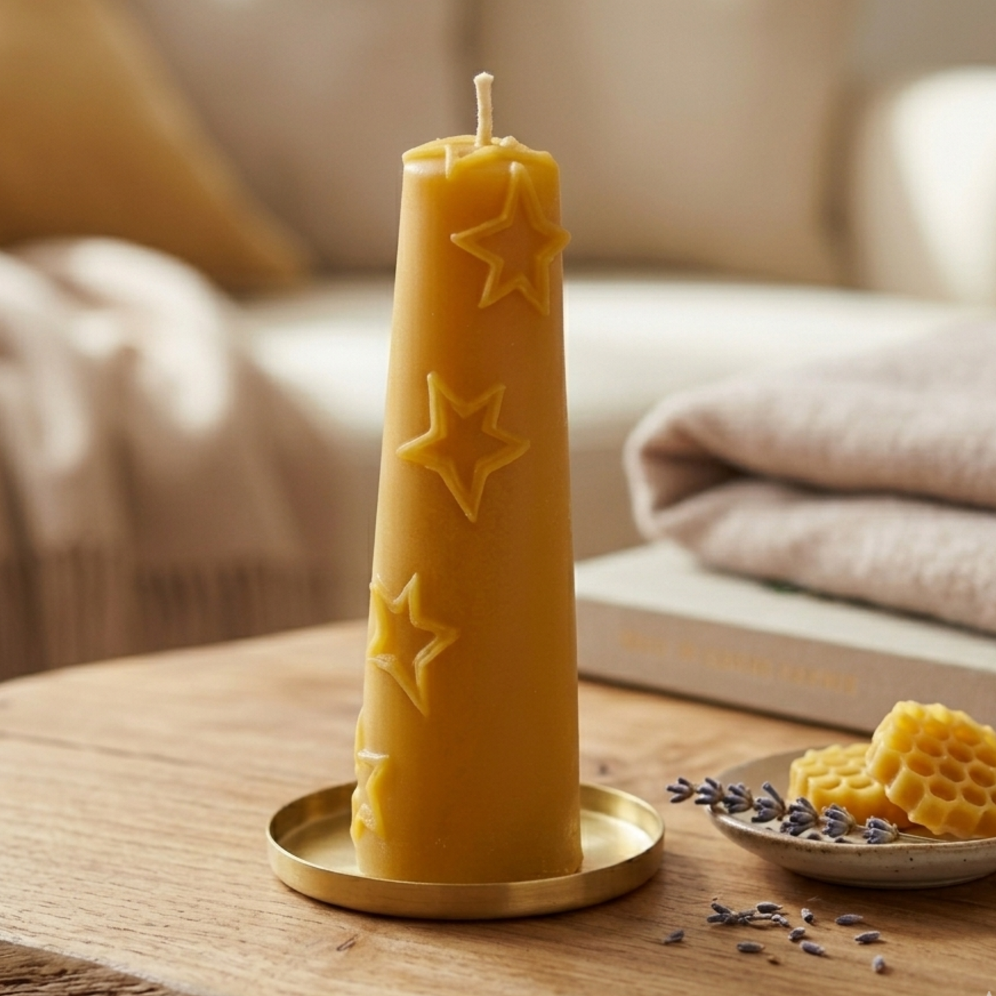Eine handgegossene Bienenwachskerze in Form einer schlanken Pyramide mit Sternenrelief auf einem massiven Holztisch. Die Kerze steht auf einem Messing-Untersetzer. Im Hintergrund ein beiges Sofa mit farblich abgestimmten Kissen. 