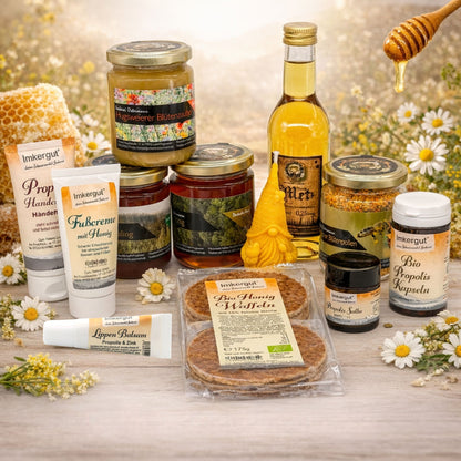 Großes Kennlernpaket der Imkerei Ostermann mit Waldhonig, Tannenhonig, Hugsweierer Blütenzauber, Blütenpollen, Mini-Honig-Met, Bio Honig Waffeln sowie Propolis Handcreme, Fußcreme, Propolis, Lippenbalsam und einer Wichtelkerze auf einem Tisch mit Blütenhintergrund. 