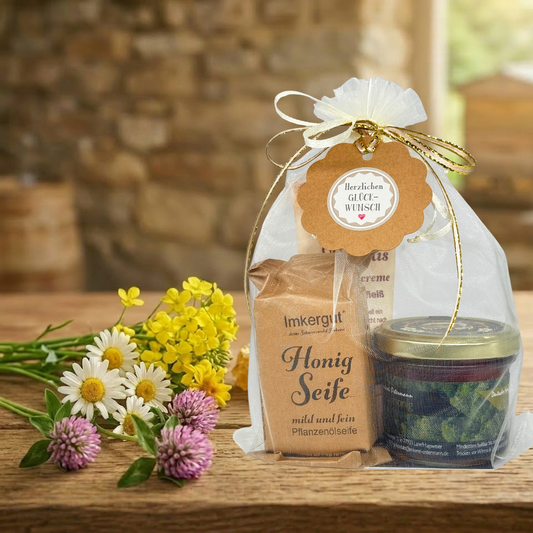 Natur-Handpflege der Imkerei Ostermann bestehend aus: 150g Waldhonig, Honig Seife und Propolis Handcreme auf einem Holztisch mit Blumen als Deko.