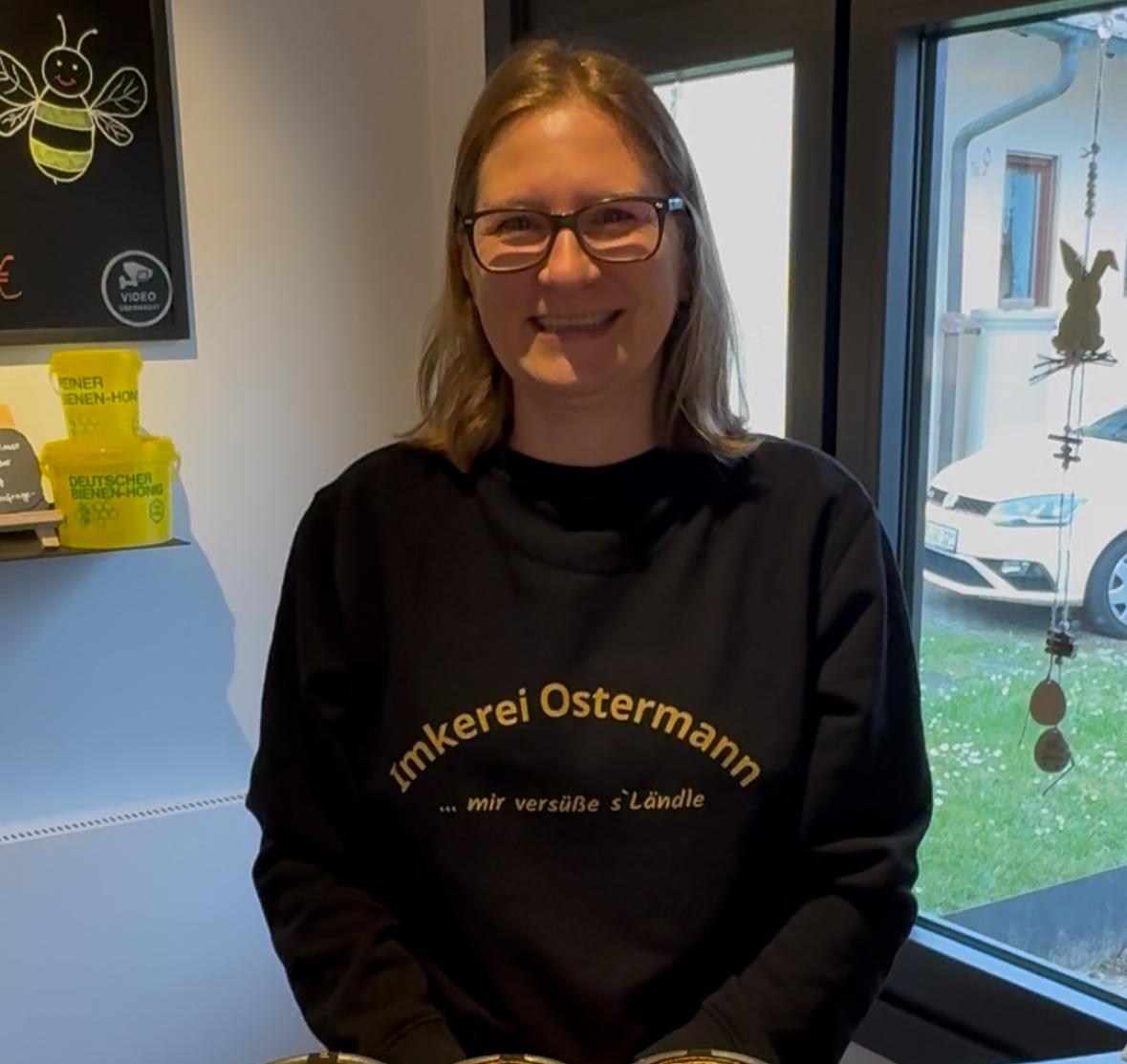 Sandra Ostermann lächelt im Hofladen der Imkerei Ostermann, wo sie Kunden berät und Honiggeschenke zusammenstellt.