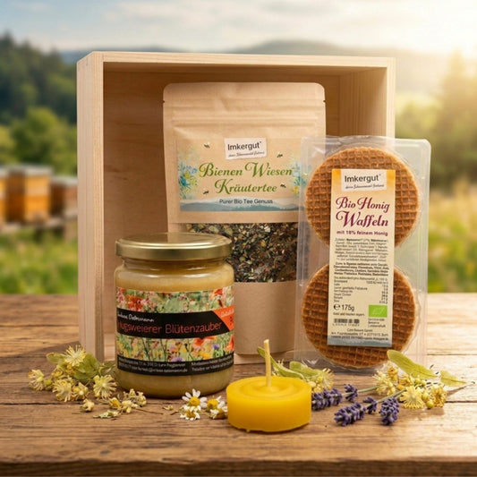 Produktbild des Geschenksets ‚Süße Auszeit‘ der Imkerei Ostermann mit einem Glas Hugsweierer Blütenzauber Honig (340g), einer Packung Bienen Wiesenkräutertee (50g) und einer Packung Bio-Honigwaffeln (175g) auf einem rustikalen Holztisch vor einem unscharfen Schwarzwald-Hintergrund, dekoriert mit Kamillenblüten und Lavendel.